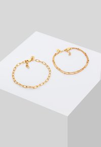 Two gold bracelets on a white surface. One features elongated links, while the other has fine chains with small beads. Both have clasp fasteners.