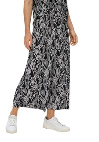 Schwarz-weiße gemusterte weite Hosen mit Falten und floralem Design. Kombiniert mit weißen Sneakers für einen lässigen Look.