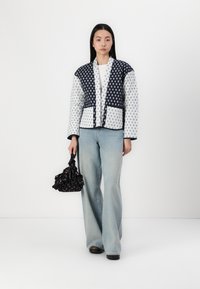 Quilted jacket with navy and white polka dot pattern, long sleeves, and contrasting trim. Paired with light blue flared jeans and a black bag.