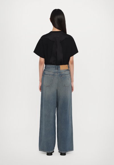 Top nero a maniche corte con una texture liscia, abbinato a jeans in denim blu chiaro a gamba larga con una toppa in pelle marrone e tasche posteriori.