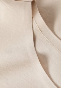 Beige kangas sileda tekstuuri ja kerge sära, millel on kaarjas kaelus ja nähtavad õmblused äärtes.
