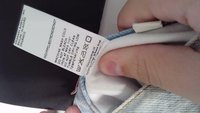 Una mano tiene un capo in denim che mostra un'etichetta bianca con istruzioni di lavaggio e contenuto dei tessuti in più lingue.