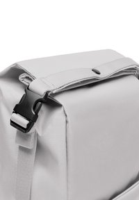 Sac à dos gris en tissu texturé, avec un dessus plat et une boucle en plastique noir. Présente un design simple et fonctionnel avec des bretelles réglables.