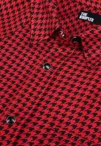 Chemise à motif pied-de-poule rouge et noir avec des boutons-pression noirs et une étiquette de marque "The Kooples" visible près du col.