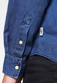 Koszula z długim rękawem, mankietami na guziki i jasnoniebieskim kolorem. Na lewej stronie znajduje się tkana metka z napisem "Originals".