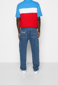 Polo a maniche corte in blu, rosso e bianco; abbinato a pantaloni cargo blu con tasche e logo sul retro. Sneakers bianche.