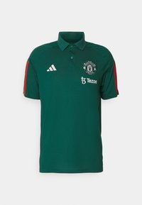 Zelené polo tričko s žebrovaným límcem, vybavené bílými pruhy Adidas, logem Manchester United a červenými akcenty na rukávech.