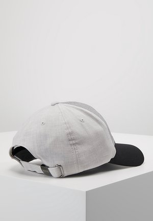 Casquette de baseball gris clair et noire avec bande métallique réglable et œillets de ventilation posée sur une surface blanche.