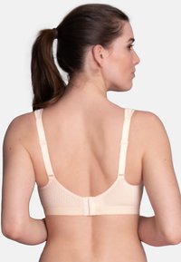 Light beige bra with breathable dotted material, adjustable straps, and a hook-and-eye closure. Smooth texture and seamless design.