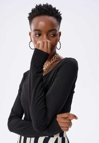 Czarny długi rękaw top z gładkiego materiału, z okrągłym dekoltem i dopasowanymi rękawami. Noszony z masywną biżuterią z złotego łańcucha.