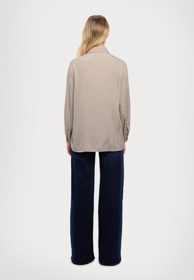 Beige long-sleeve shirt with a subtle vertical stripe pattern, rounded collar, relaxed fit, paired with dark blue wide-leg pants.