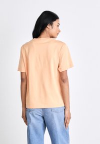 Pfirsichfarbene Baumwoll-T-Shirts mit lässigem Schnitt, kurzen Ärmeln und Rundhalsausschnitt. Rücken ohne Verzierungen, kombiniert mit hellblauen Jeans.