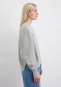 Felpa grigia con vestibilità rilassata, polsini a costine e colletto a girocollo. Presenta spacchi laterali all'orlo per maggiore comfort. Abbinata a jeans blu.