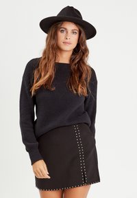 Un pull noir en peluche avec des manches longues associ�é à une jupe noire. La jupe présente une rangée de clous en argent sur un côté et une fente à l'avant.