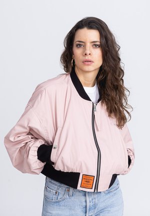 Hellrosa Bomberjacke mit einem schwarzen gerippten Kragen und Bündchen, ausgestattet mit einem Reißverschluss und einem orangefarbenen Etikett am vorderen Saum.