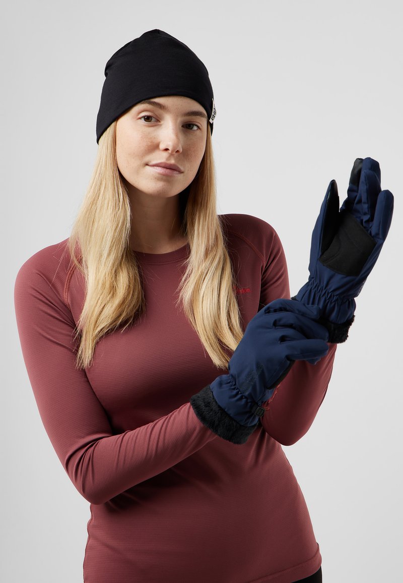 Guanti blu navy con palmi neri testurizzati e polsini foderati in pelliccia. Modello che indossa un top a maniche lunghe color bordeaux e un berretto nero.