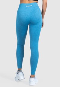 Leggings blu realizzati in un tessuto elastico e testurizzato presentano un alto elastico in vita con il nome del brand "SMILODOX" sul retro. Indossati con scarpe bianche.