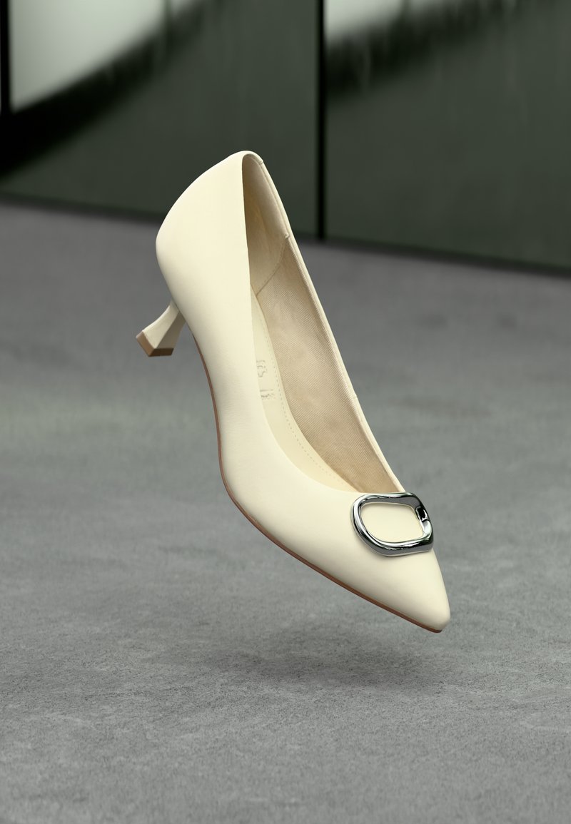 Chaussure blanche en cuir à bout pointu avec un accent de boucle en argent et un petit talon épais, présentée sur une surface grise texturée.