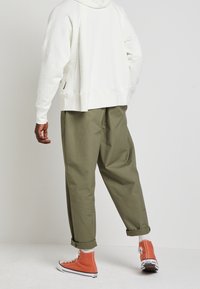 Bílá mikina s uvolněným střihem, kombinovaná s olivovými kalhotami s širokými nohavicemi. Oranžové tenisky s bílou podrážkou. Jednoduché, ležérní oblečení.