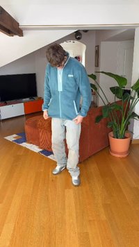 Svjetloplava flis jakna sa zatvaračem sprijeda i bočnim džepovima, nošena uz svijetle traperice i srebrne tenisice, na drvenoj podlozi.