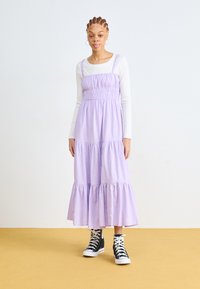 Rochie maxi tiered în lavandă, cu talie elastică, asortată cu adidași negri înalți. Rochia are bretele subțiri și un croi lejer.