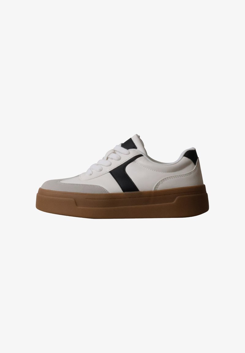 Baskets blanches avec accents noirs, lacets blancs et semelle épaisse en caoutchouc marron, vues de profil sur un fond uni.