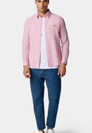 Maglietta a maniche lunghe a righe rosse e bianche con chiusura a bottone, dotata di un piccolo logo, abbinata a jeans blu e sneaker bianche.