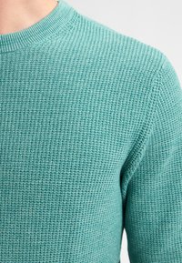 Turkooise gebreide trui met een gestructureerd patroon, voorzien van een geribde halslijn en zachte, ademende stof.