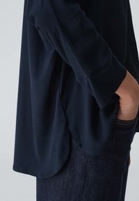 Maglietta a maniche lunghe blu navy con orlo rotondo, tessuto morbido e dettagli con spacco laterale, abbinata a jeans di denim scuri.