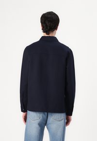 Navyblauwe shirt met een kraag, lange mouwen en knoopmanchetten. Soepele textuur en een rechte snit, met een yoke-detail op de achterkant.