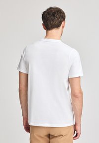 Vit t-shirt med kort ärm i bomull, rund halsringning, slät yta och utan synliga mönster eller tryck. Bilden visar baksidan.