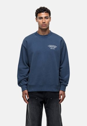Donkerblauwe sweatshirt met een ronde hals, losse pasvorm en lange mouwen. Kenmerkt zich door witte bedrukte tekst op de borst en ribgebreide manchetten en zoom.