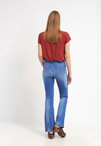 Top corto rojo de manga corta, jeans azules acampanados y zuecos de madera marrones. Tejido suave con bolsillos traseros y detalles de costura sutiles.