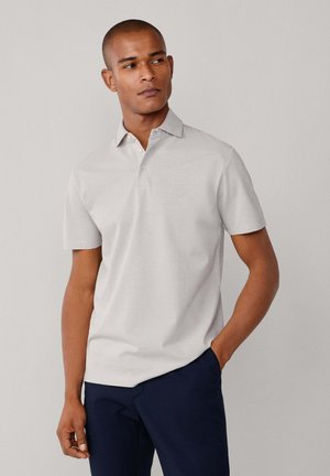 Polo gris claro con cuello clásico, mangas cortas y tres botones. Tela suave, diseño ajustado, combinado con pantalones azul marino oscuro.
