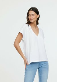 Haut blanc à manches courtes en V, fabriqué à partir d'un tissu léger, avec un design ample et une texture lisse. Associé à un jean bleu clair.