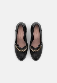 Scarpe slip-on in pelle nera con una catena dorata decorativa sul ponte, dotate di una soletta rosa chiaro e un design della punta arrotondata.