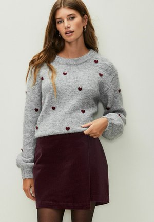 Gray knit sweater with red heart embellishments, paired with a dark burgundy corduroy skirt. Sweater has a round neckline and loose sleeves.