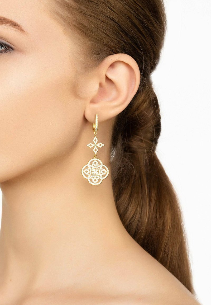 Gold hoop earrings featuring intricate geometric designs and a floral motif, accented with small embellishments, hanging near the earlobe.