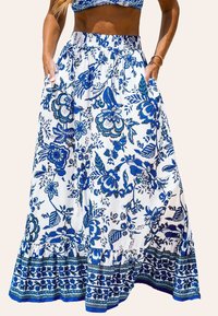 Lange, gelaagde rok van witte stof met een blauw bloemenpatroon. Beschikt over een rekbare tailleband en zijzakken. Gerafeld zoomdetail.