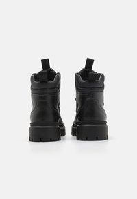 Botas negras hasta el tobillo hechas de cuero liso, con un cuello acolchado, tiradores y suelas de goma gruesas con patrones estriados para mayor tracción.