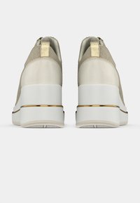 Beiget tennarit, joissa on teksturoitu päällinen, valkoinen korokepohja ja metalliset kultaiset yksityiskohdat. Takakuva näyttää vetokahvan ja sileän pinnan.