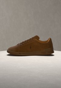 Καφέ δερμάτινο sneaker με κορδόνια, με χαμηλή σόλα και λογότυπο Polo στο πλάι, τοποθετημένο πάνω σε ανοιχτή επιφάνεια με μονόχρωμο φόντο.
