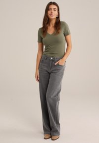 Haut à col en V à manches courtes vert olive, associé à un jean gris taille haute, ample, avec poches avant et fermeture à bouton.