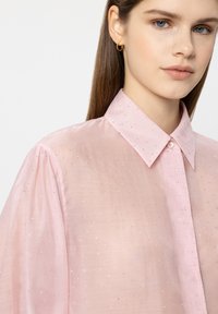 Pink sheer blouse with a structured collar, featuring silver dot details, a button front, and puffed long sleeves. Smooth texture.