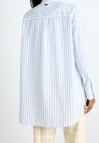 Oversized košile s dlouhým rukávem v světle modrých a bílých proužcích, s kulatým spodním lemem, vyrobená z hladké látky.