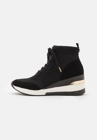 Zapatillas altas con cuña en negro, con parte superior de punto, acentos de ante y una franja metálica dorada en la suela. Presenta cordones y un zipper lateral.
