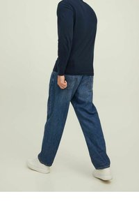 Maglietta a maniche lunghe navy, jeans in denim blu a taglio comodo e sneaker bianche. Cuciture a vista, design a quattro tasche e silhouette rilassata.
