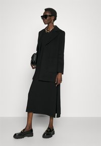 Sort oversized blazer med sjalskrave, parret med en knælang sort kjole. Sorte chunky loafers med guldhardware og en struktureret håndtaske.