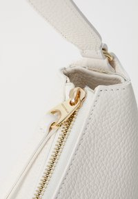 Borsa a tracolla bianca in pelle con superficie texturizzata, hardware con zip dorata e tracolla liscia. Interno di colore chiaro. Il tirante della zip presenta il marchio.