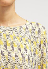 Haut à rayures jaune et gris avec un décolleté carré, présentant un tissu texturé et un motif géométrique de formes et de lignes variées.